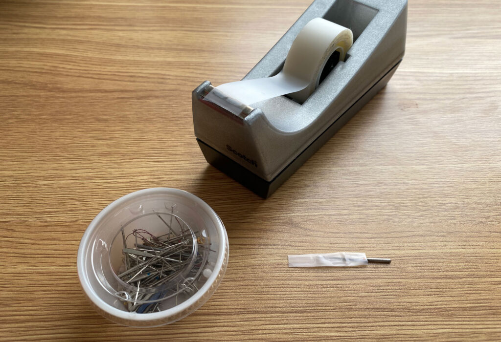 a lidded container, a tape dispenser and a needle wrapped in tape ready to be disposed